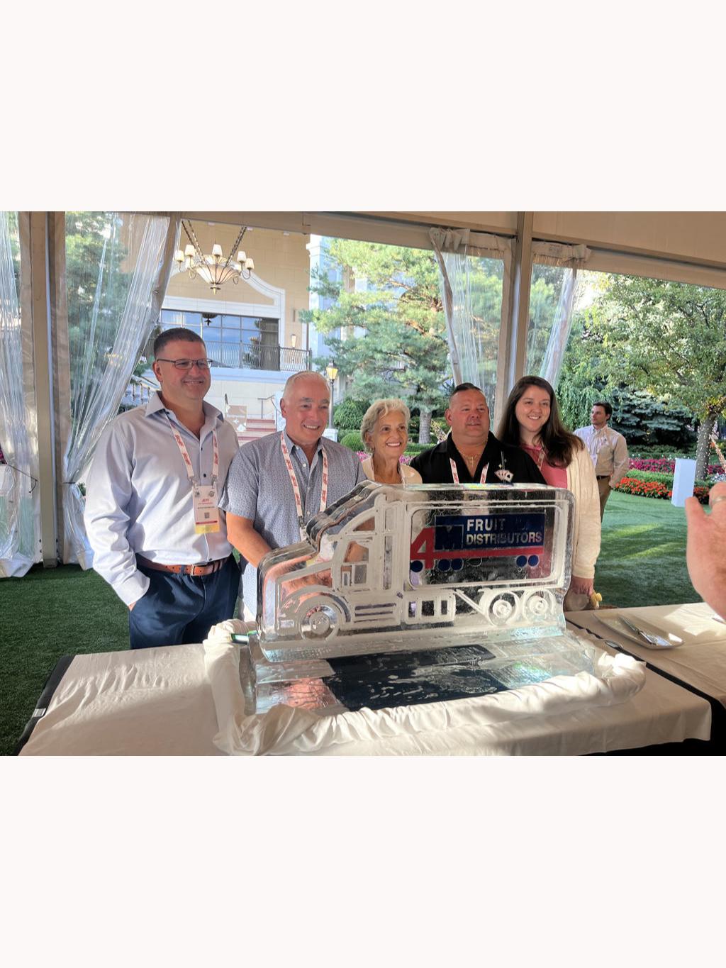 Group of people at an outdoor event celebrating with a cake and a film clapboard.